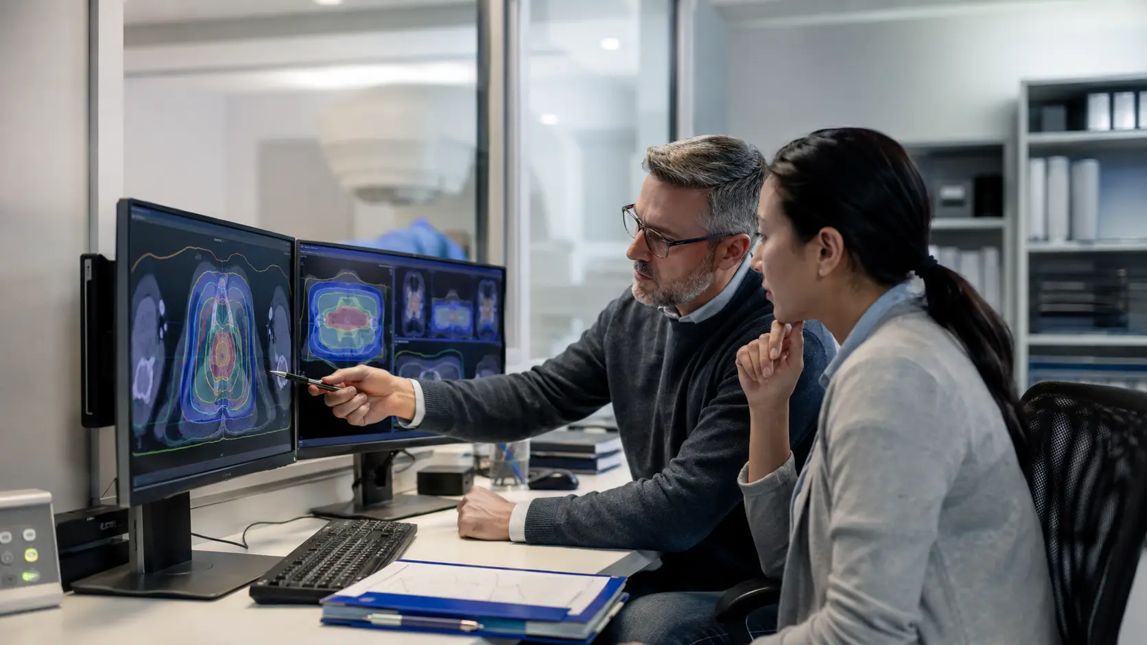 A medical dosimetrist and medical physicist review abstract treatment-planning images on two monitors.