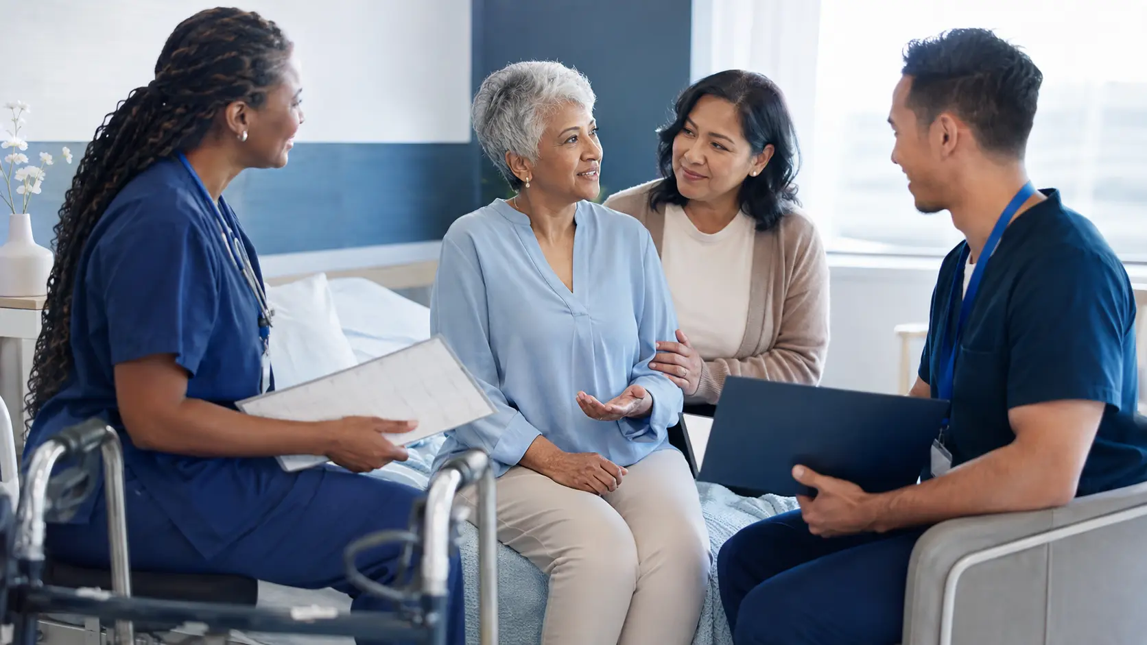 Older adult, family caregiver, nurse, and rehabilitation clinician completing a respectful hospital-to-home handoff.