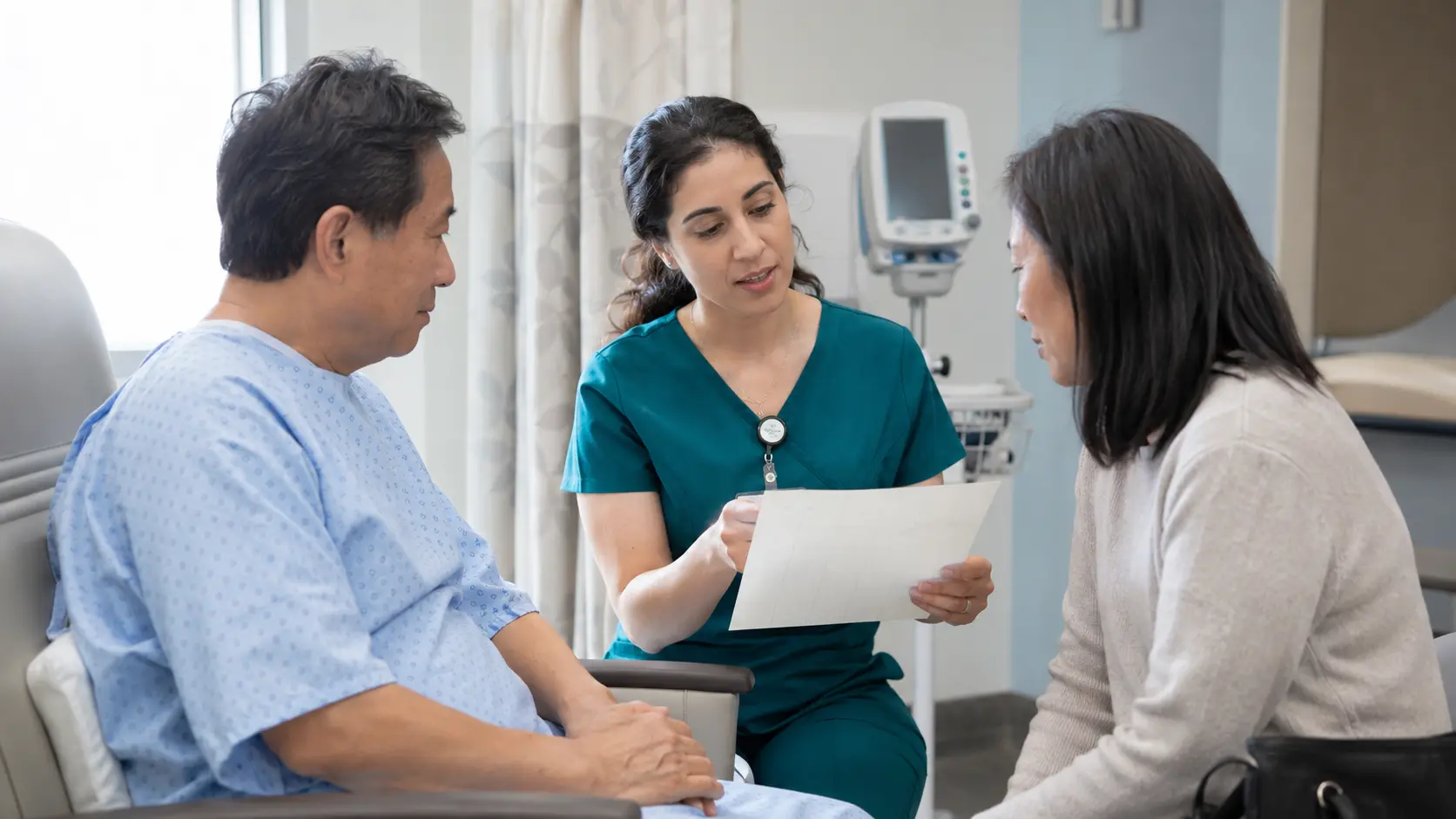 Perianesthesia nurse reviewing readiness with an adult patient and caregiver in a bright preoperative bay