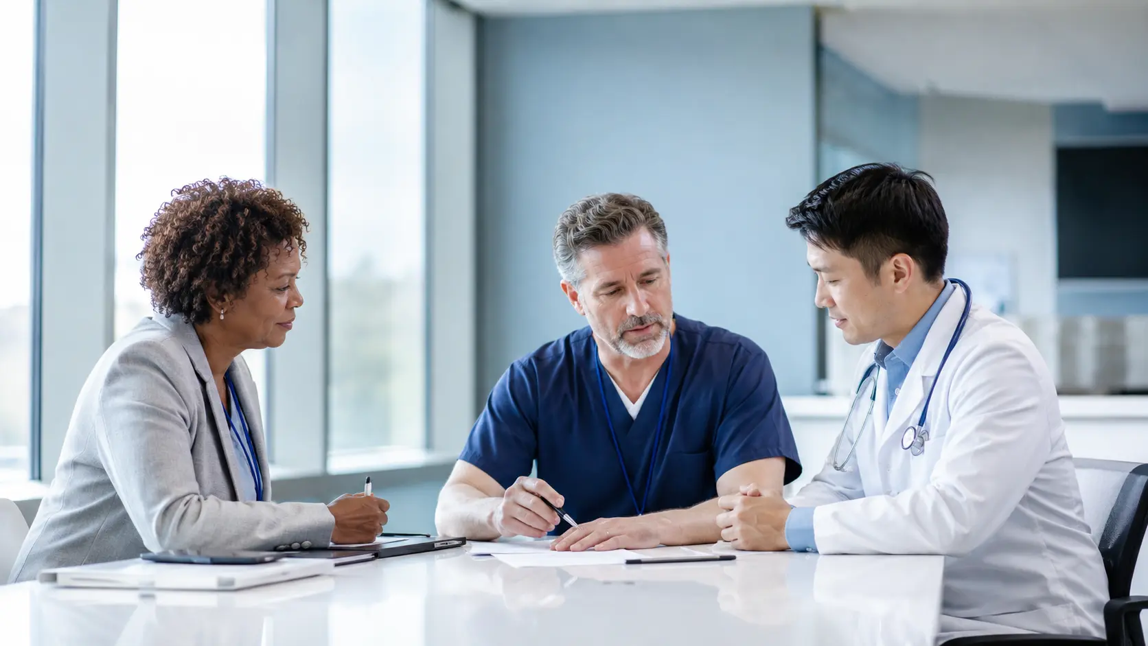 Three healthcare professionals reviewing assignment readiness together in a bright conference area.