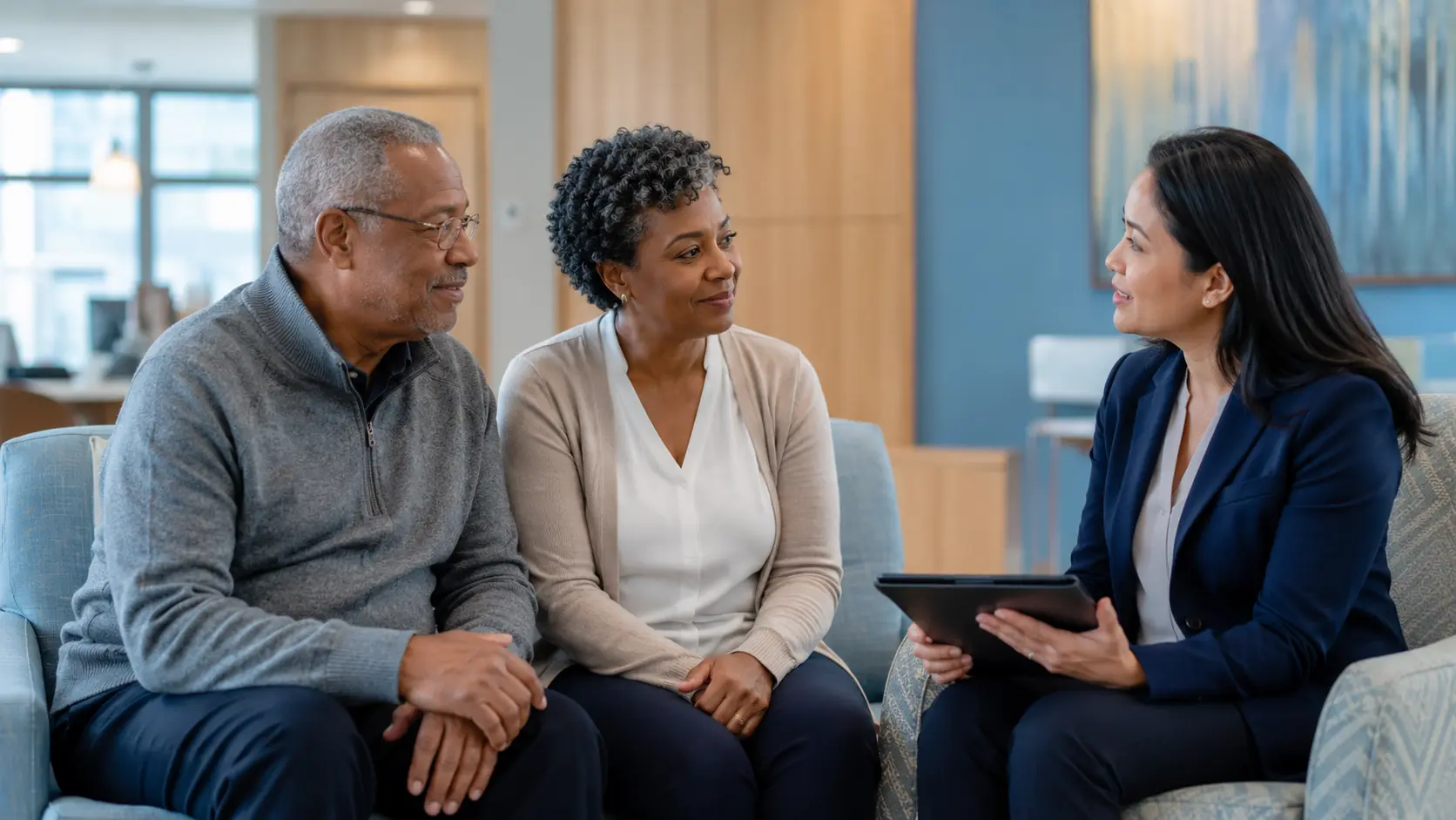 An older adult patient and caregiver having a respectful conversation with a patient navigator in an accessible outpatient setting.