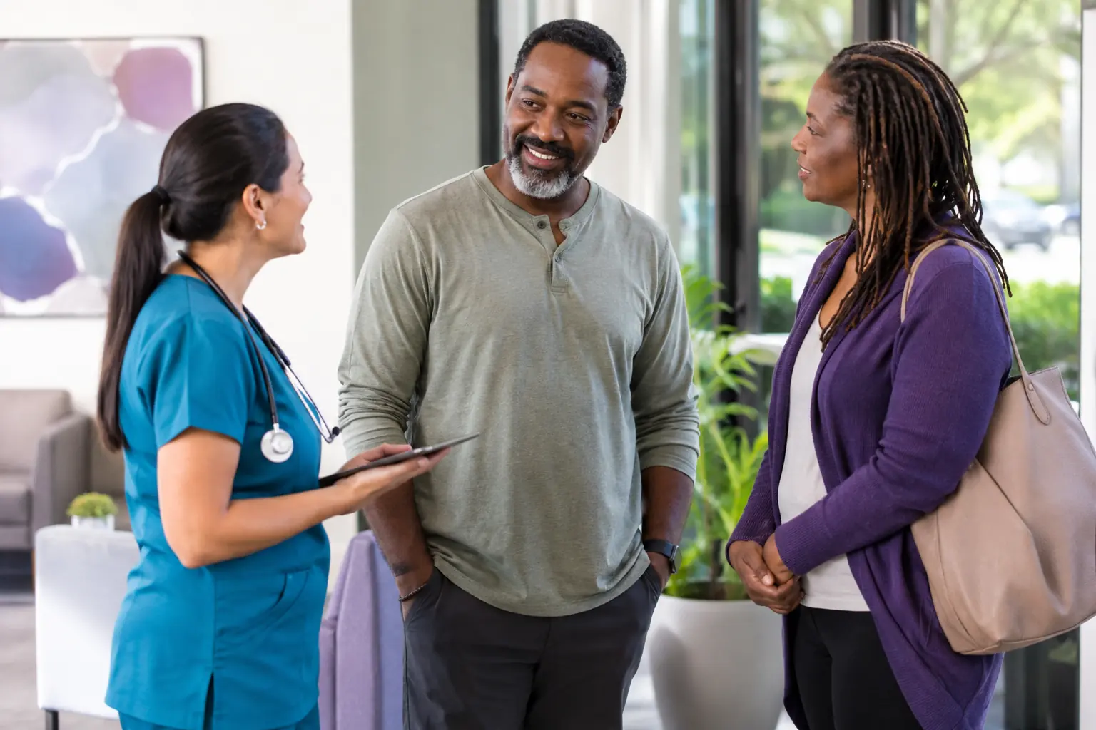 An adult standing with a nurse and a community support professional during a warm handoff in a clinic.