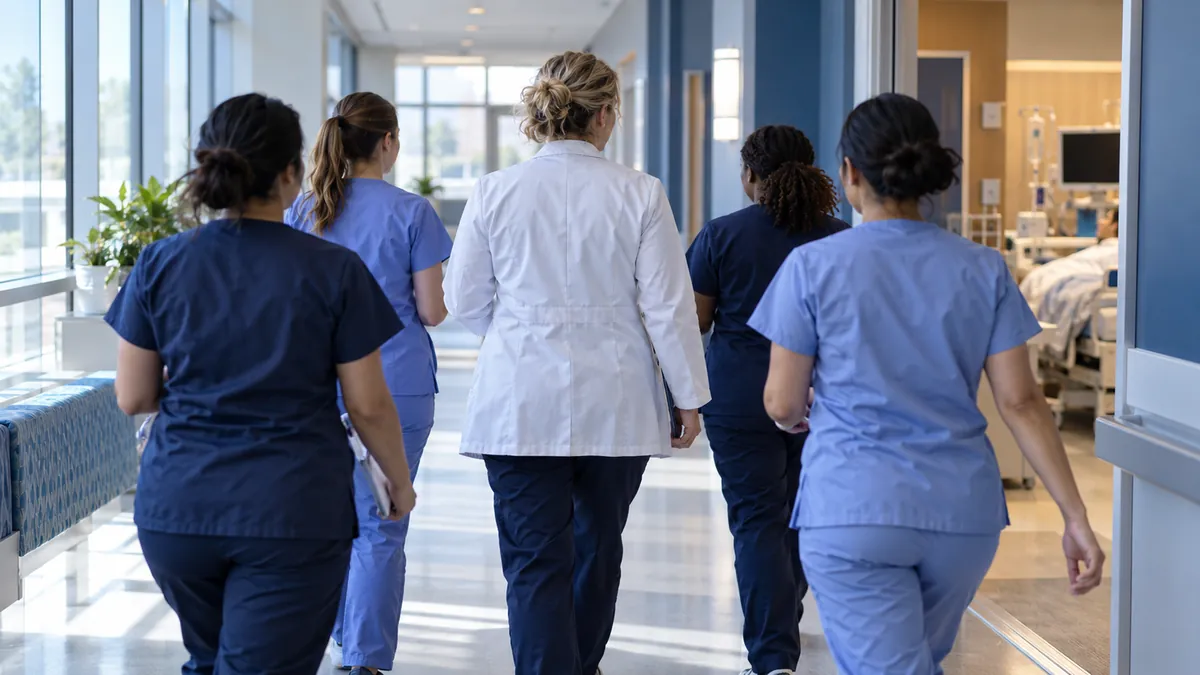 The clinical nurse specialist walks with a group of nurses down a bright hospital hallway toward a patient room.